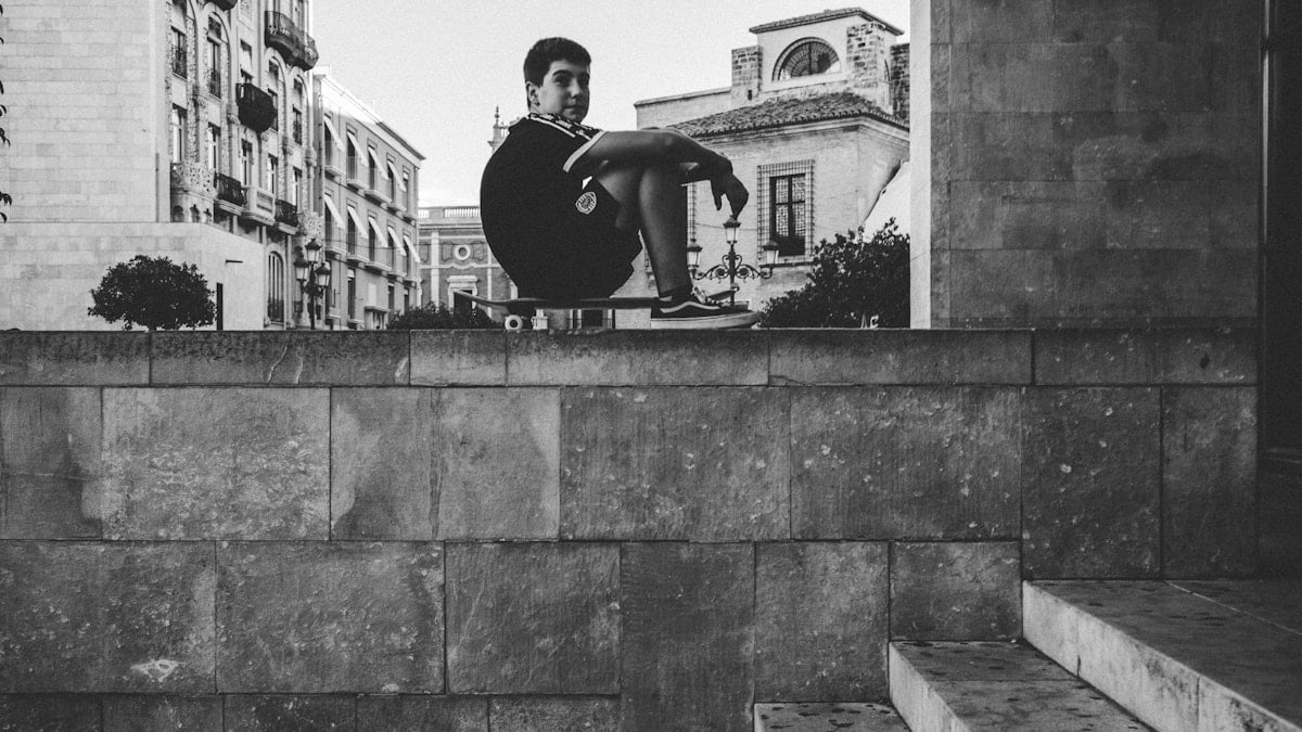 grayscale photo of man sitting skateboard
